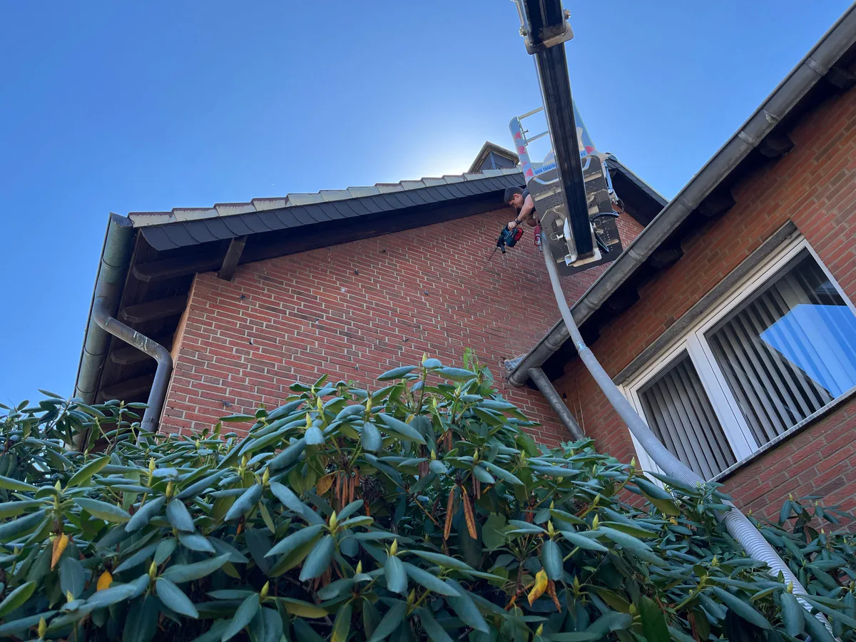 Monteur auf einer Hebebühne bläst Dämmstoff in eine Klinkerfassade ein